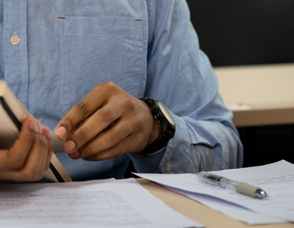 Close up shot of hands flipping a notebook at a desk with papers and a pen